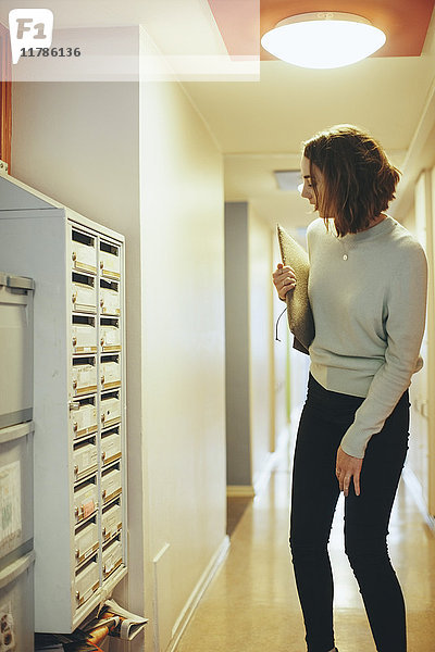Frau hält Dokument in der Hand und schaut auf den Briefkasten im Flur