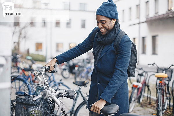 Fröhlicher junger männlicher Student steht mit dem Fahrrad in der Stadt