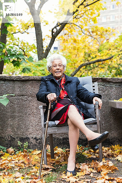 Ganzkörperporträt einer glücklichen Seniorin auf einem Stuhl im Park