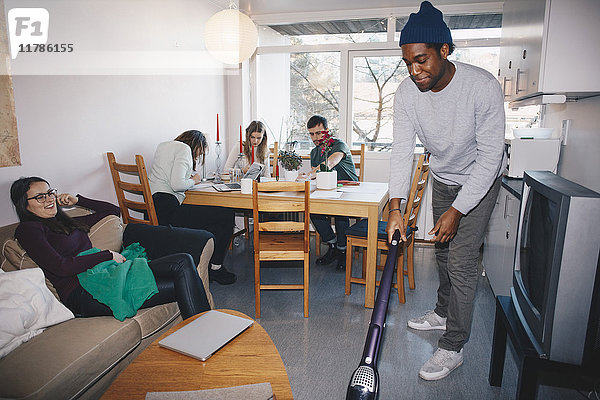 Mann putzt den Boden  während Freunde im Studentenwohnheim sitzen.