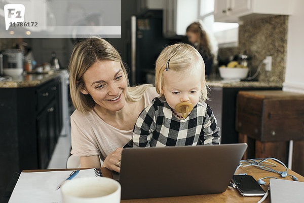 Glückliche Mutter mit Tochter mit Laptop mit Familie im Hintergrund zu Hause