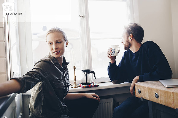 Paar sitzt in der Küche und trinkt zu Hause Kaffee am Fenster.