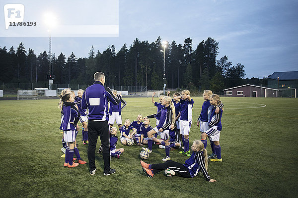 Coach erklärt mit Mädchen Fußballmannschaft auf dem Feld gegen den Himmel