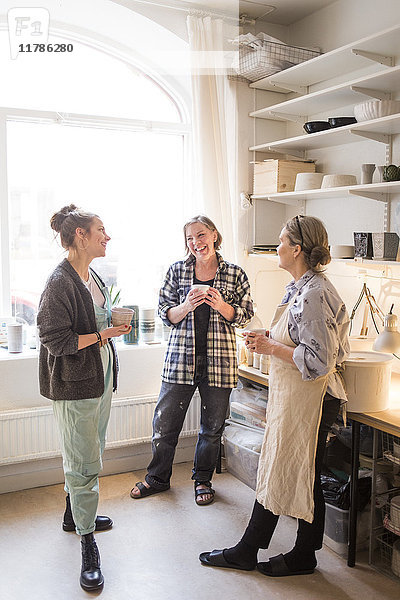Zufriedene Kolleginnen stehen mit Kaffeebechern im Keramikgeschäft