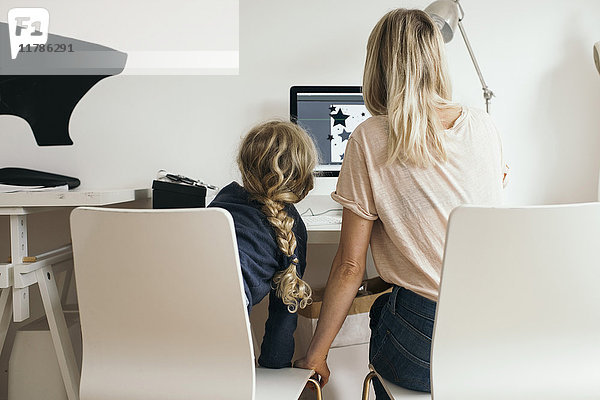 Rückansicht des Mädchens mit Mutter bei der Benutzung des Laptops zu Hause