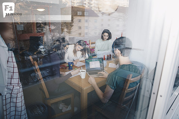 Junge Freunde beim gemeinsamen Lernen im Studentenwohnheim durch ein Glasfenster gesehen
