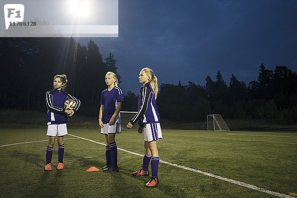 Mädchen  die in der Abenddämmerung auf dem Fußballplatz gegen den Himmel stehen.
