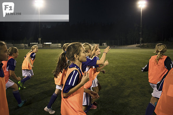 Mädchen  die nachts auf dem beleuchteten Fußballplatz laufen