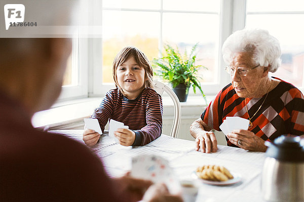 Glücklicher Junge beim Kartenspielen mit Urgroßeltern zu Hause