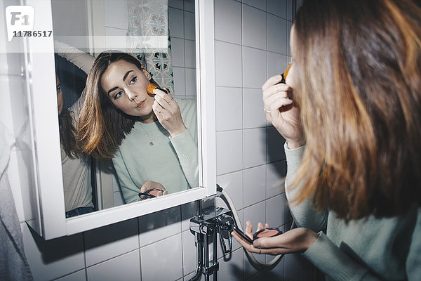 Junge Frau  die errötet  schaut in den Spiegel auf das College-Badezimmer.