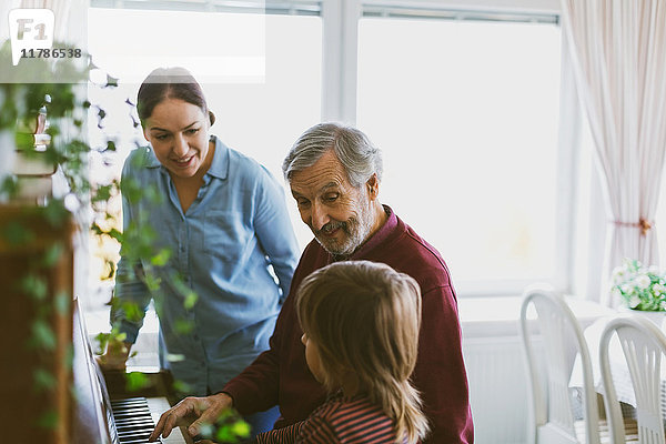 Lächelnde Mutter und Urgroßvater beim Klavierspielen im Haus