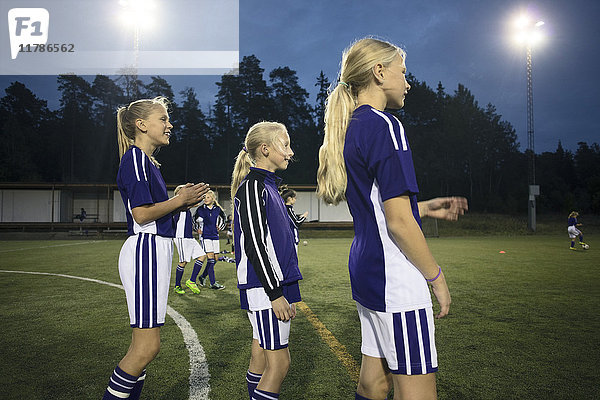 Seitenansicht der Mädchen  die in der Abenddämmerung auf dem Fußballplatz gegen den Himmel stehen.