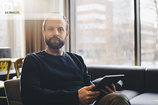 Porträt eines selbstbewussten Geschäftsmannes mit digitalem Tablett in der hell erleuchteten Bürolobby