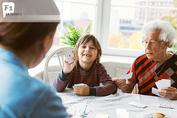 Glücklicher Junge spielt Karten mit Mutter und Urgroßmutter zu Hause.