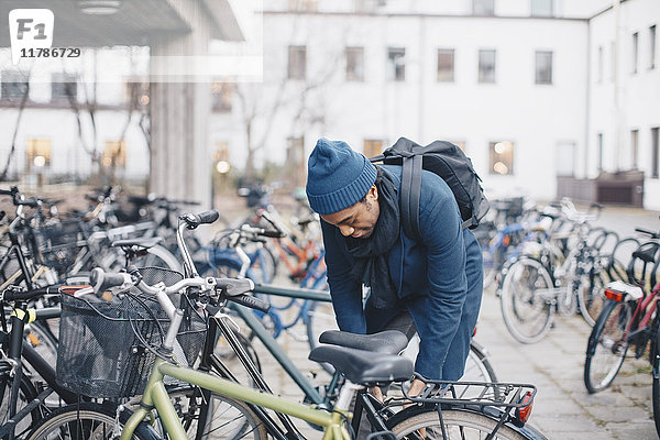 Junge männliche Universitätsstudentin entsperrt Fahrrad auf dem Campus