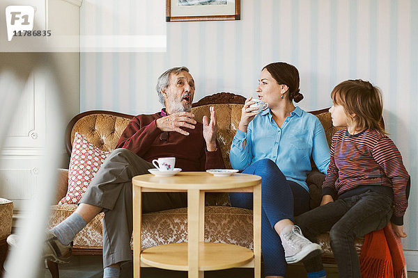 Senior Mann im Gespräch mit Tochter und Urenkel auf Sofa im Wohnzimmer