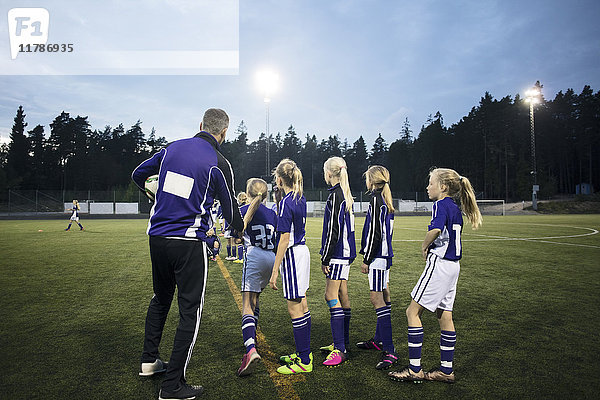 Trainerin erklärt weibliche Fußballmannschaft auf dem Feld gegen den Himmel