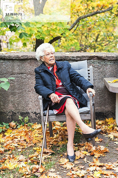Volle Länge der älteren Frau  die auf einem Stuhl im Park sitzt.