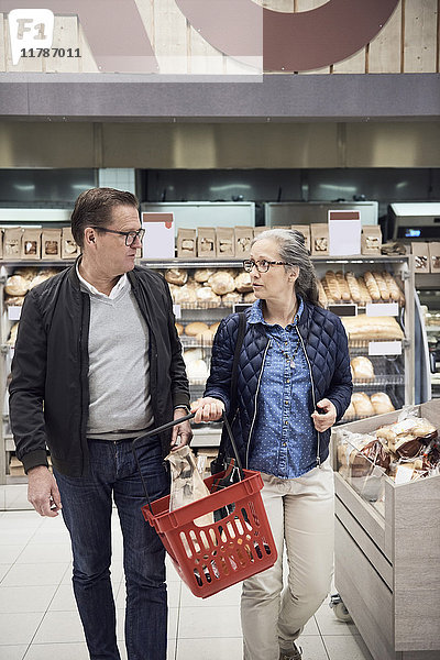 Reife Paare beim Spazierengehen mit dem Korb im Supermarkt