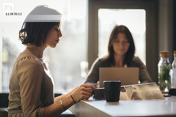 Seitenansicht der Geschäftsfrau beim Lesen des Dokuments am Schreibtisch mit Mitarbeiter im Hintergrund