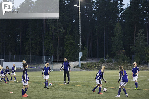 Trainer  der Mädchen beim Fußballspielen auf dem Spielfeld beobachtet.