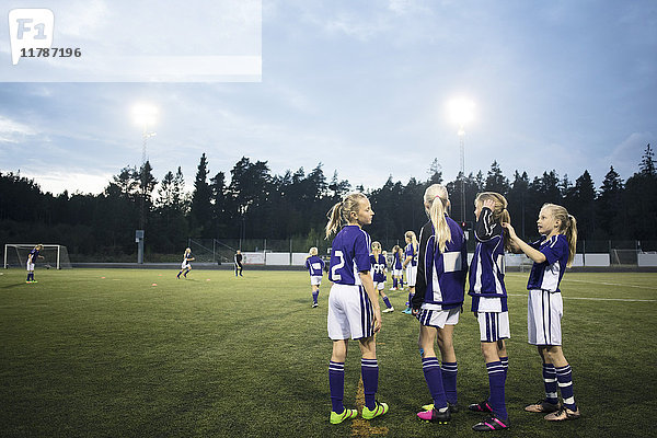 Mädchen stehen auf dem Fußballfeld gegen den Himmel