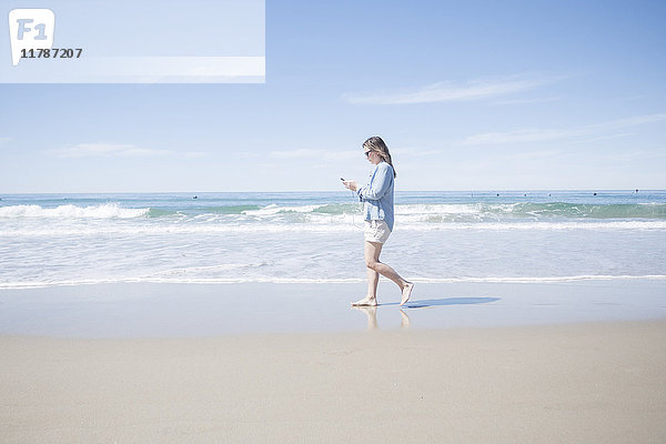 Vollständige Seitenansicht der reifen Frau mit dem Handy beim Spaziergang am Strand