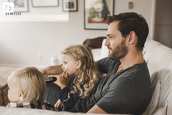 Mittlerer erwachsener Vater mit Töchtern  die zu Hause im Wohnzimmer fernsehen.