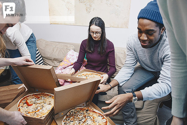 Hochwinkelansicht von jungen Freunden beim Öffnen von Pizzakartons im Schlafsaal