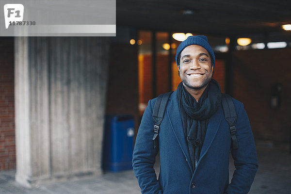 Porträt eines glücklichen Mannes in blauer warmer Kleidung und Strickmütze auf dem Campus