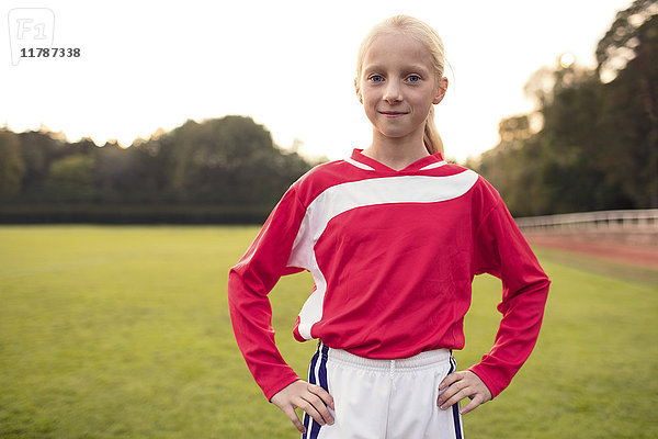 Porträt eines selbstbewussten Mädchens  das mit den Händen an der Hüfte auf dem Fußballfeld steht.