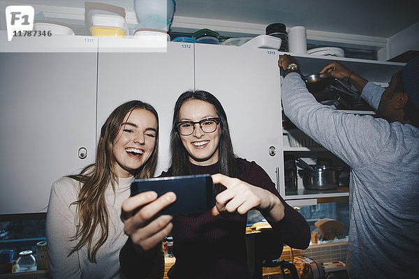 Glückliche Frauen genießen mit dem Handy von Mann in der Küche im Studentenwohnheim