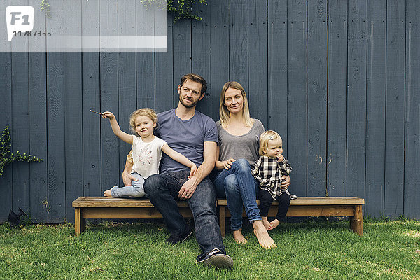 Portrait von glücklichen Eltern und Kindern  die auf Sitzen gegen den Zaun im Hof sitzen.