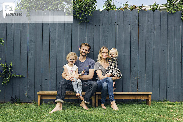 Porträt von glücklichen Eltern und Kindern  die auf Sitzen gegen den Zaun auf dem Hof sitzen