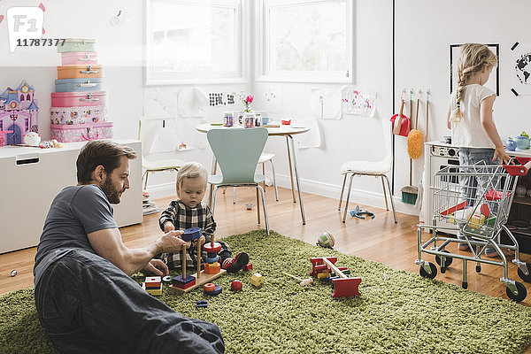 Vater und Töchter spielen mit Spielzeug im Spielzimmer zu Hause