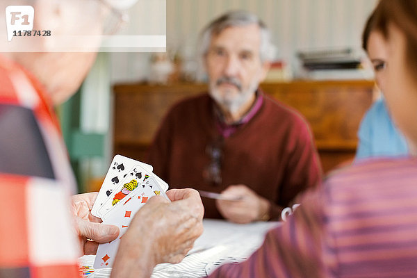 Abgeschnittenes Bild einer älteren Frau  die mit ihrer Familie zu Hause Karten spielt.