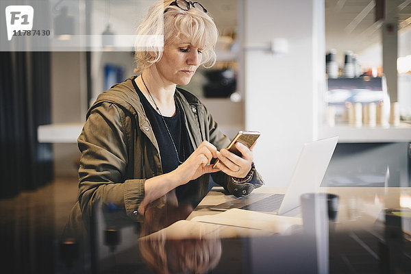 Geschäftsfrau im Büro am Schreibtisch mit Smartphone