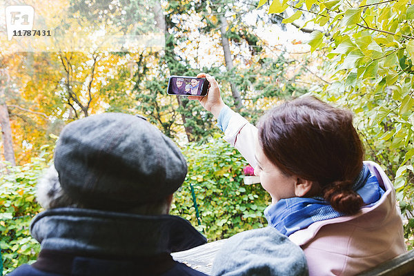 Frau nimmt Selfie durch Smartphone mit Familie im Park im Herbst
