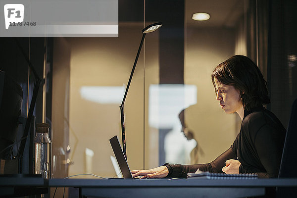 Seitenansicht der Geschäftsfrau mit Laptop am Schreibtisch im dunklen Büro