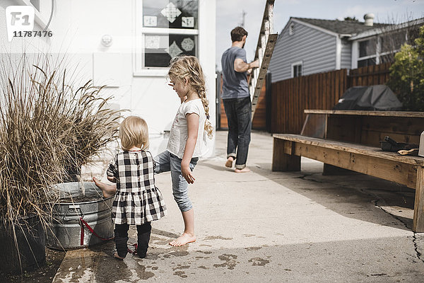 Mädchen spielen mit Wasser im Container vor dem Haus