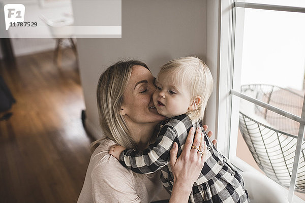 Glückliche Mutter küsst Tochter am Fenster zu Hause