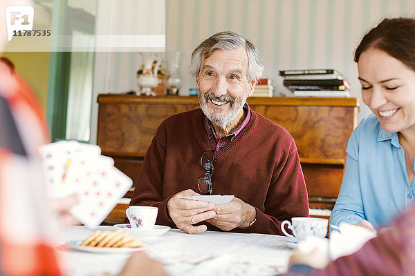 Lächelnder älterer Mann  der mit seiner Familie zu Hause Karten spielt.