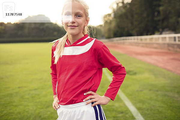 Porträt eines selbstbewussten Mädchens  das mit den Händen an der Hüfte auf dem Fußballfeld steht.