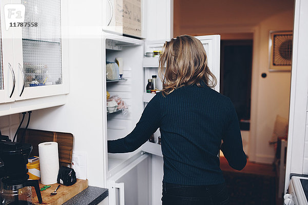 Rückansicht der Frau beim Öffnen des Kühlschranks in der heimischen Küche