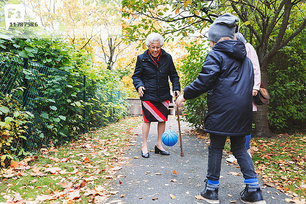 Volle Länge der Seniorin und des Urenkels  der mit dem Ball auf dem Fußweg im Park spielt.