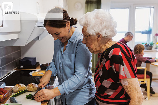 Seitenansicht der Seniorin beim Anblick der Tochter  die in der Küche Zucchini schneidet.