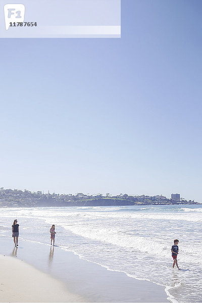Mutter mit Kindern genießt Urlaub am Strand bei klarem Himmel