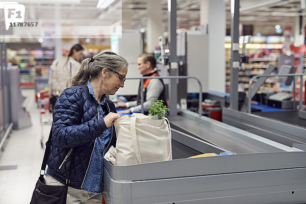 Lächelnde reife Frau mit Tasche an der Kasse im Supermarkt