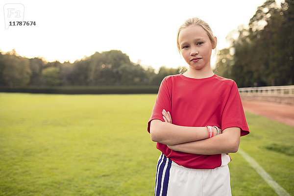 Porträt einer selbstbewussten Fußballspielerin  die mit gekreuzten Armen auf dem Feld steht.