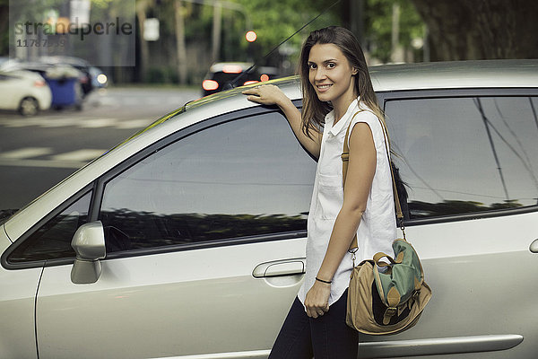 Junge Frau  die sich gegen das Auto lehnt  lächelnd